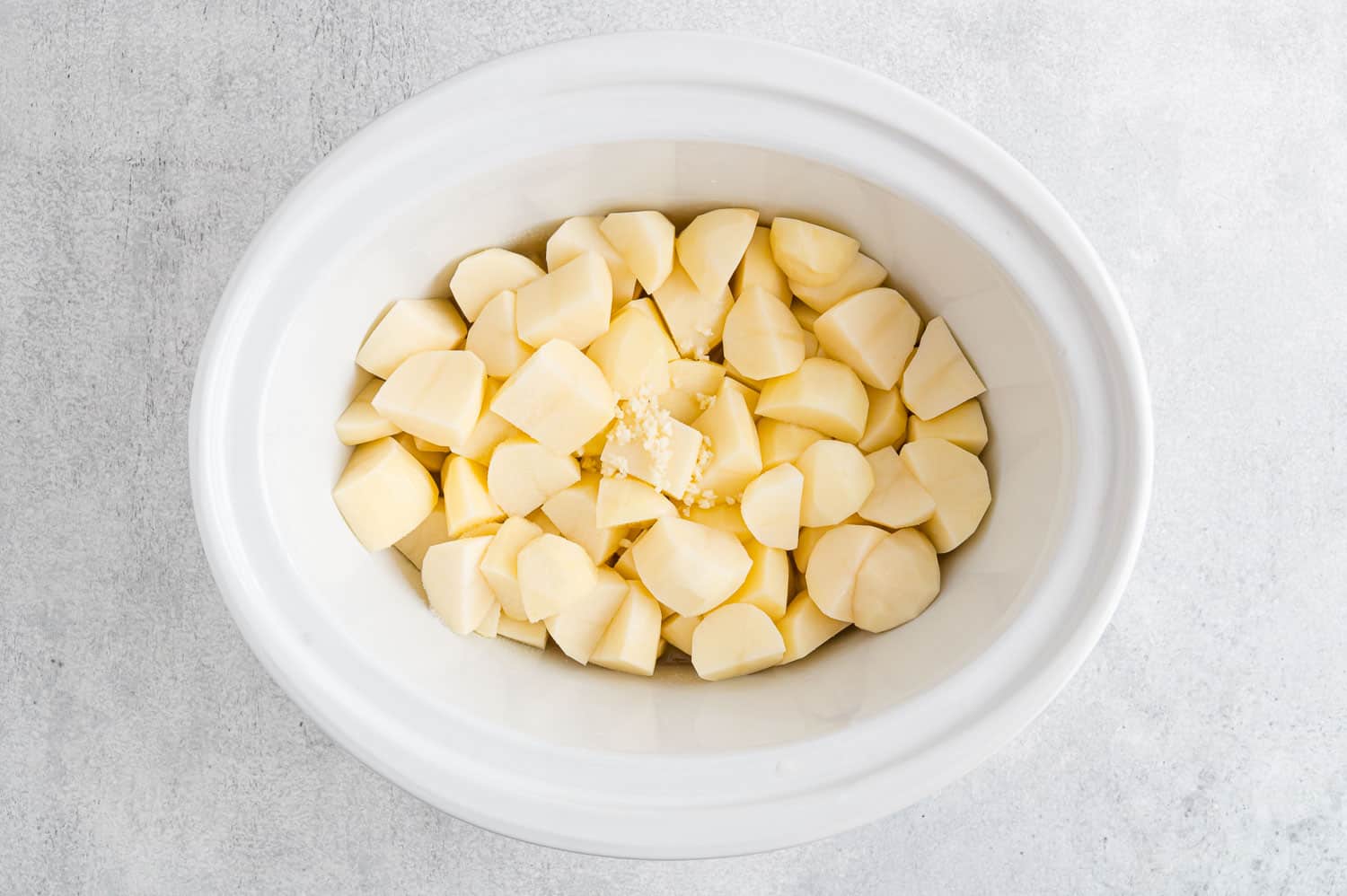 Uncooked peeled potatoes in a crockpot.