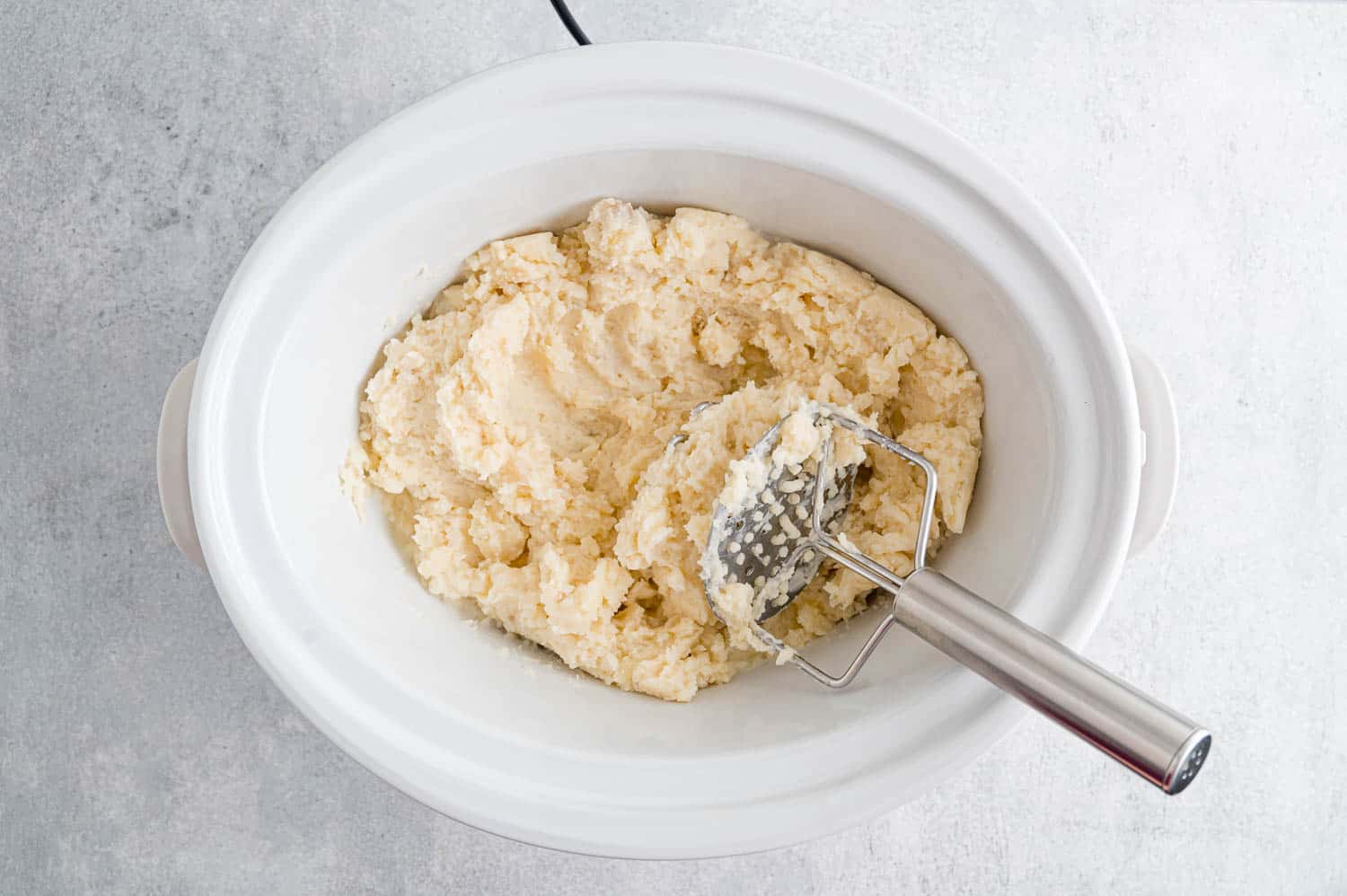 Potatoes being mashed in a slow cooker.