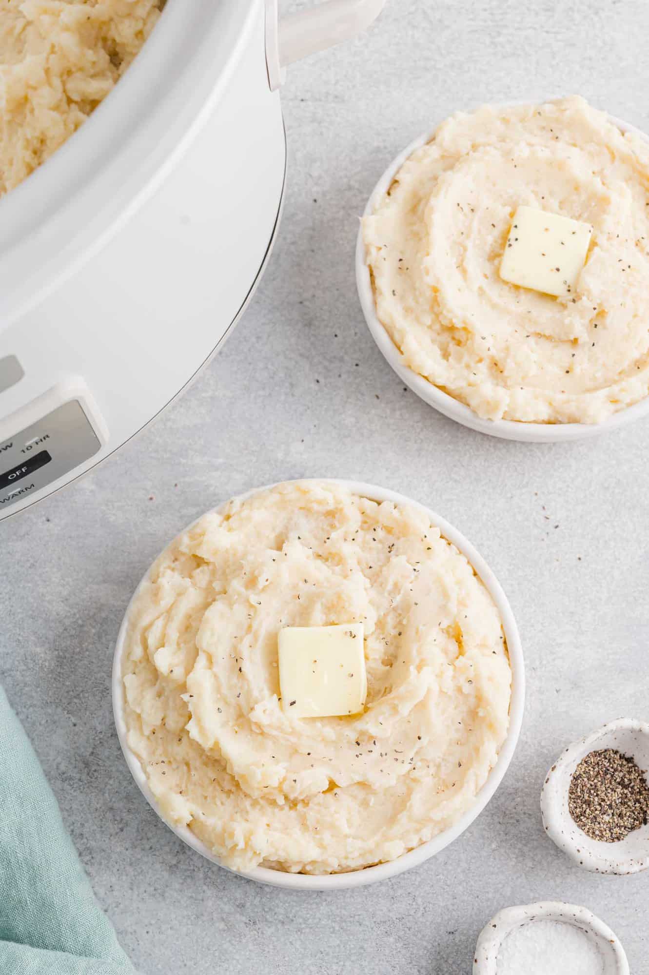 Mashed potatoes in two bowls by a crockpot.