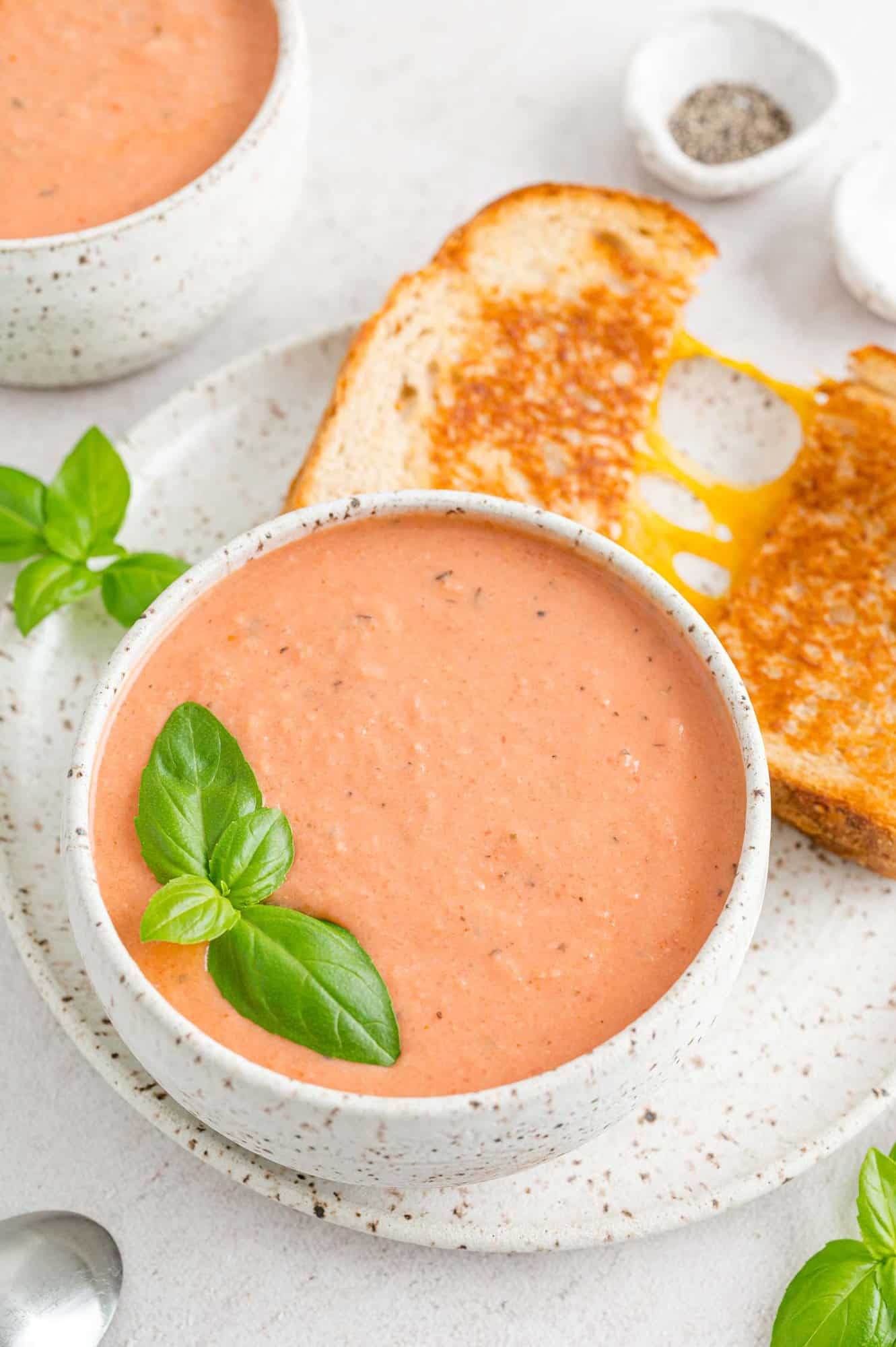 Healthy creamy tomato soup on a plate with grilled cheese.