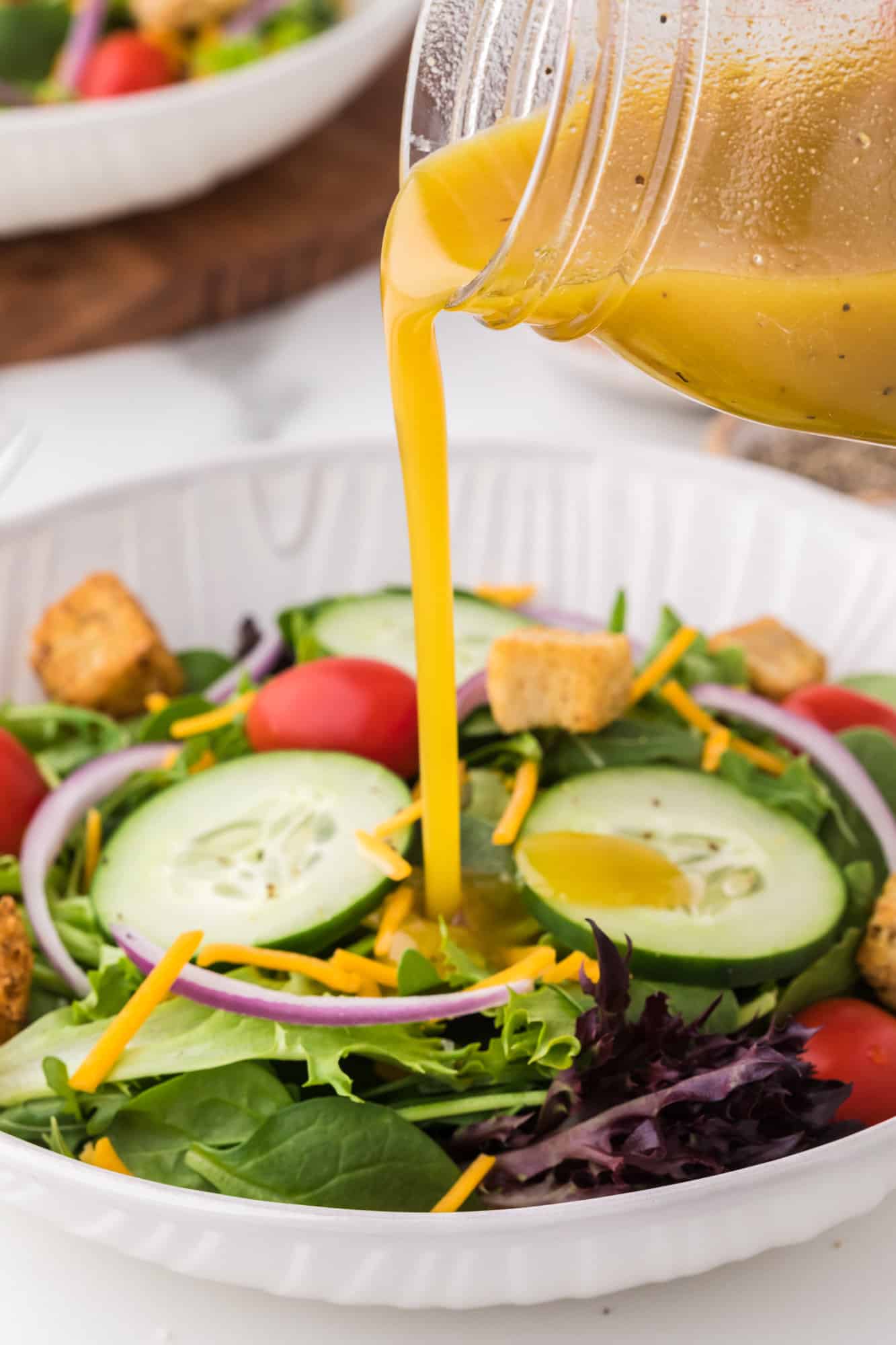Vinaigrette being poured on a green salad.