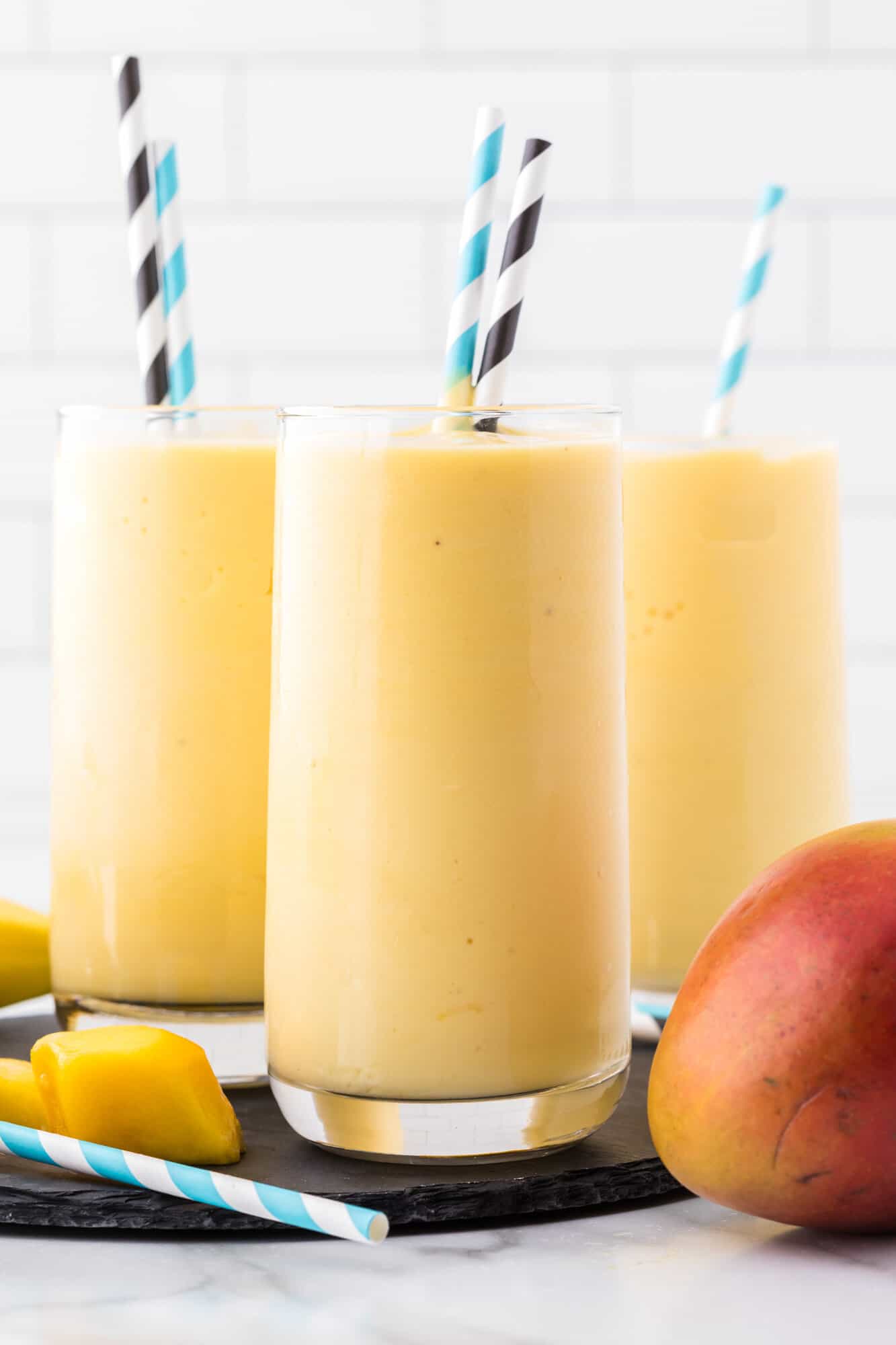 Three mango smoothies with paper straws.