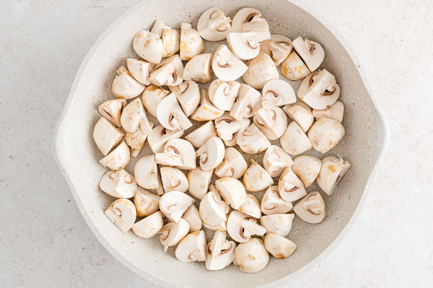 Raw mushroom quarters in pan.