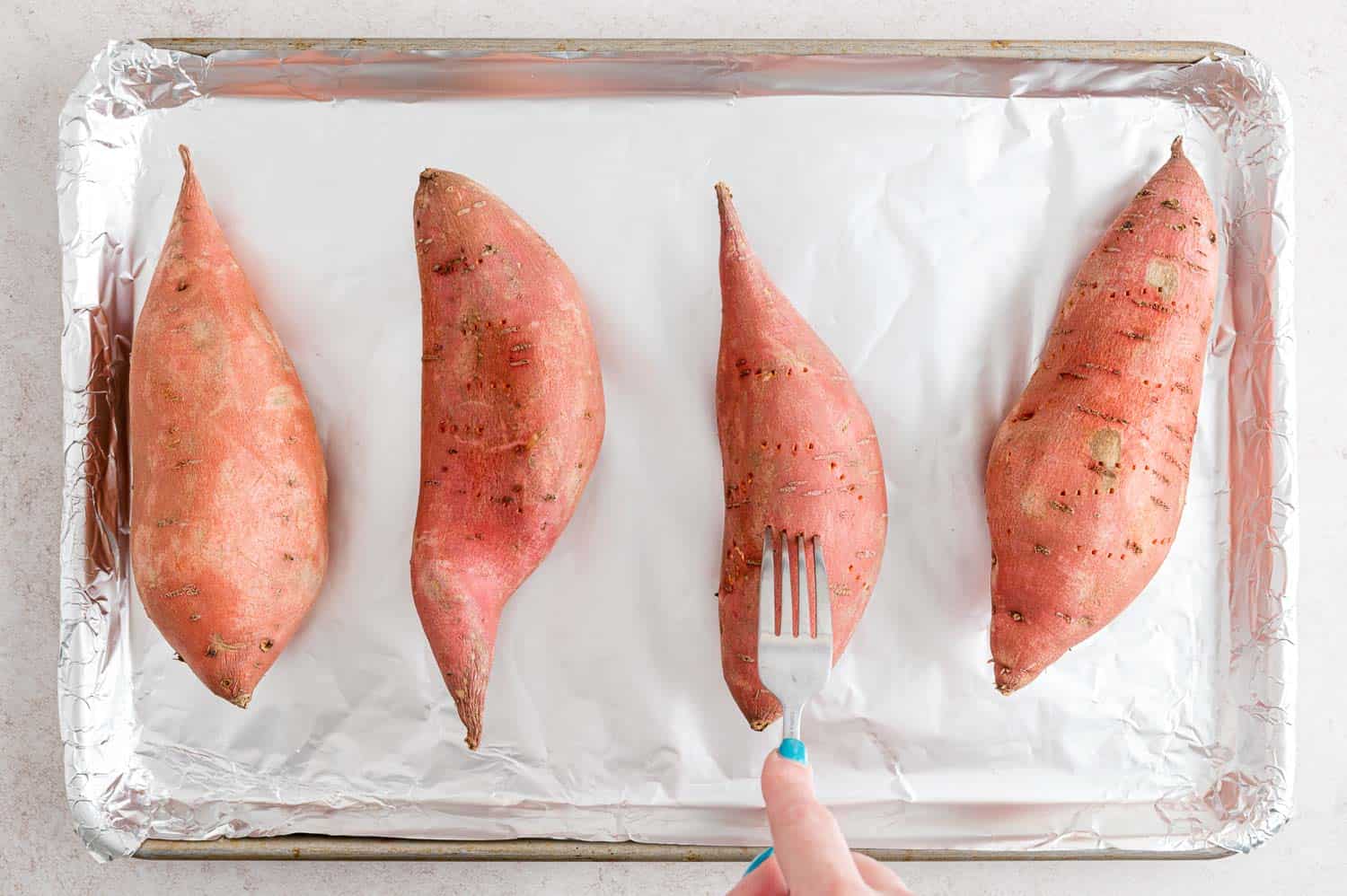 Fork poking holes in an unbaked sweet potato.