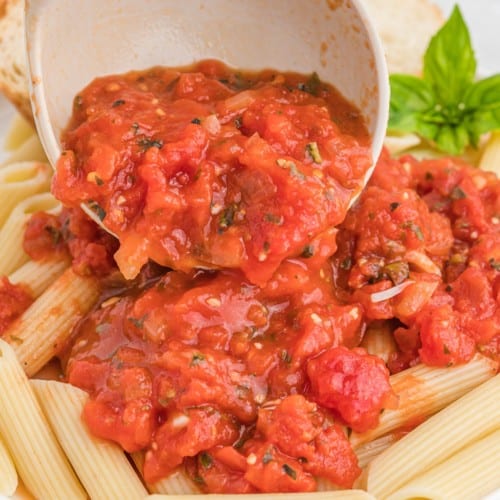 Arrabbiata sauce being scooped onto pasta.