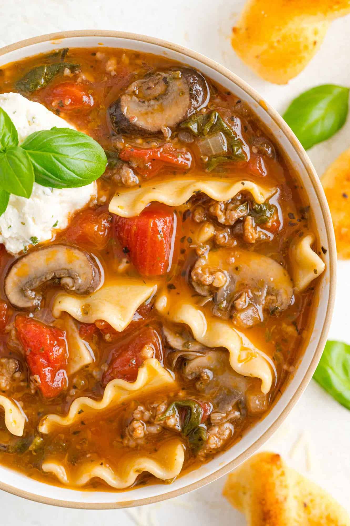 Lasagna soup in a bowl with cheese and basil garnish.