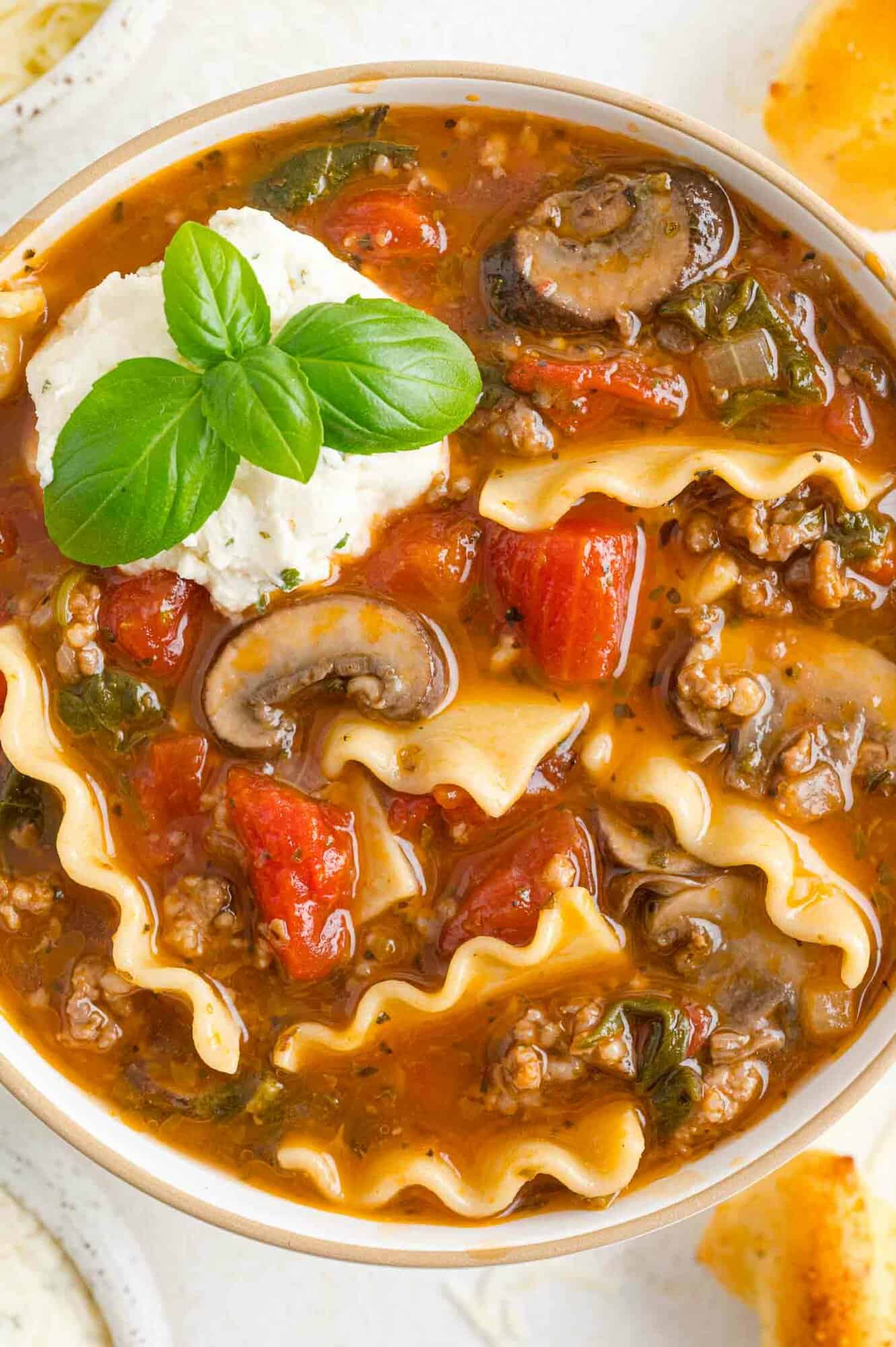 Lasagna soup with cheese and basil on top.