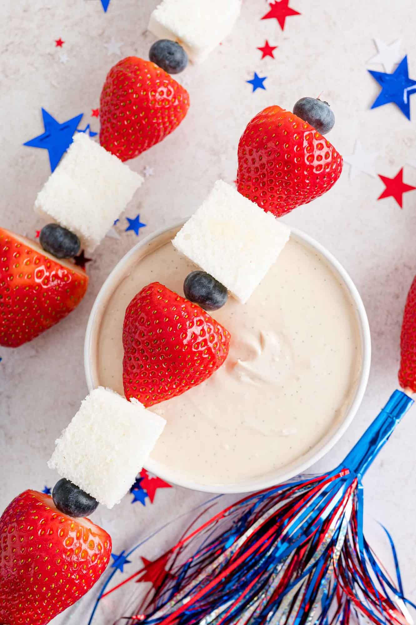 Red white and blue fruit skewer placed on top of bowl of yogurt dip.