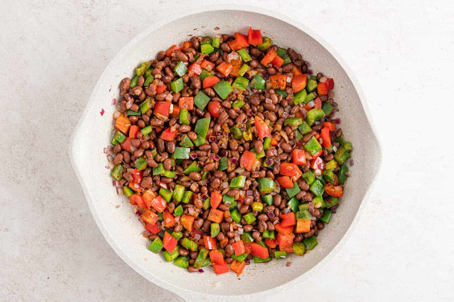 Peppers and onions with black beans and taco seasoning in a frying pan.