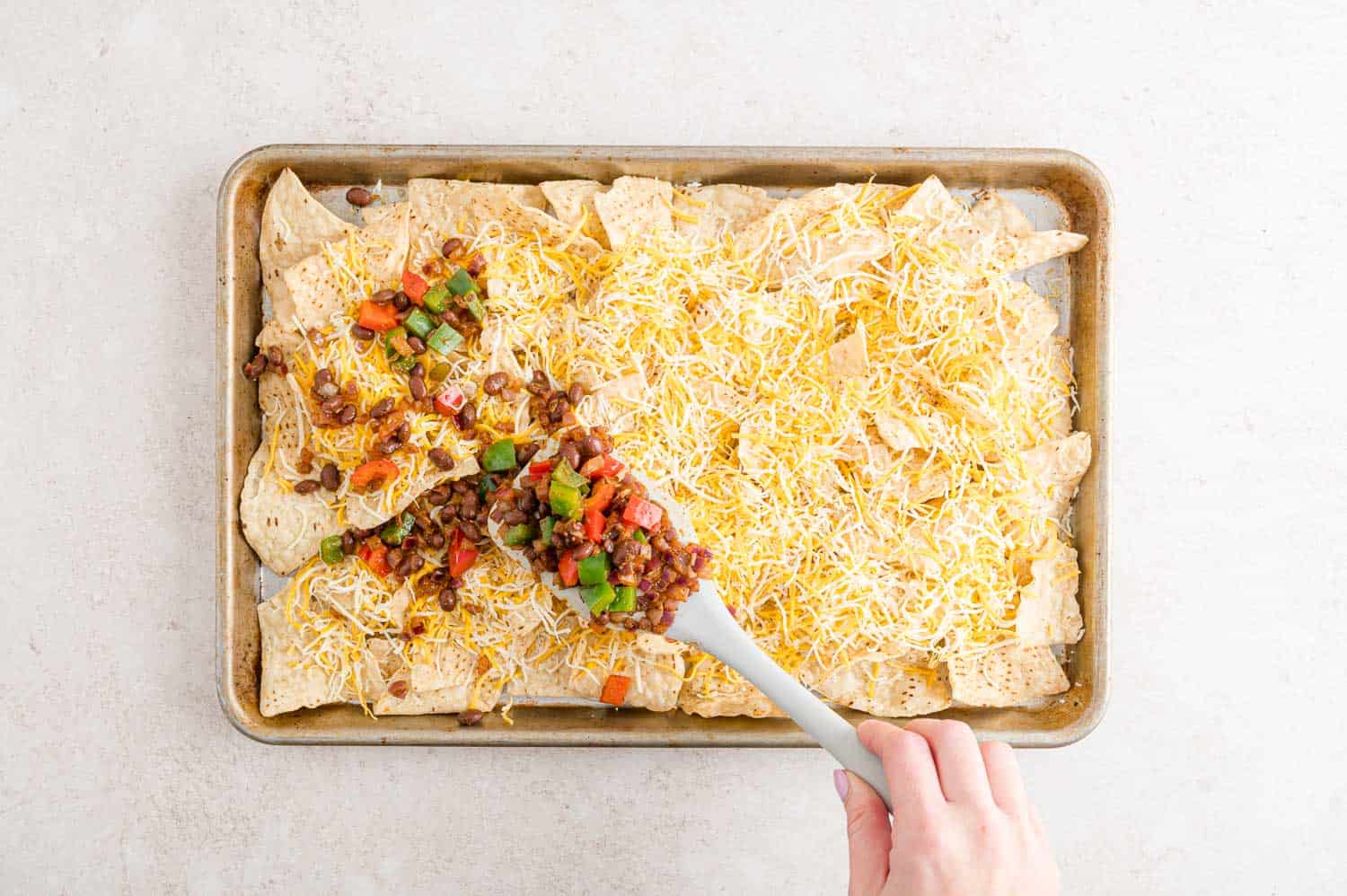 Peppers, onions, and beans being added to nachos.