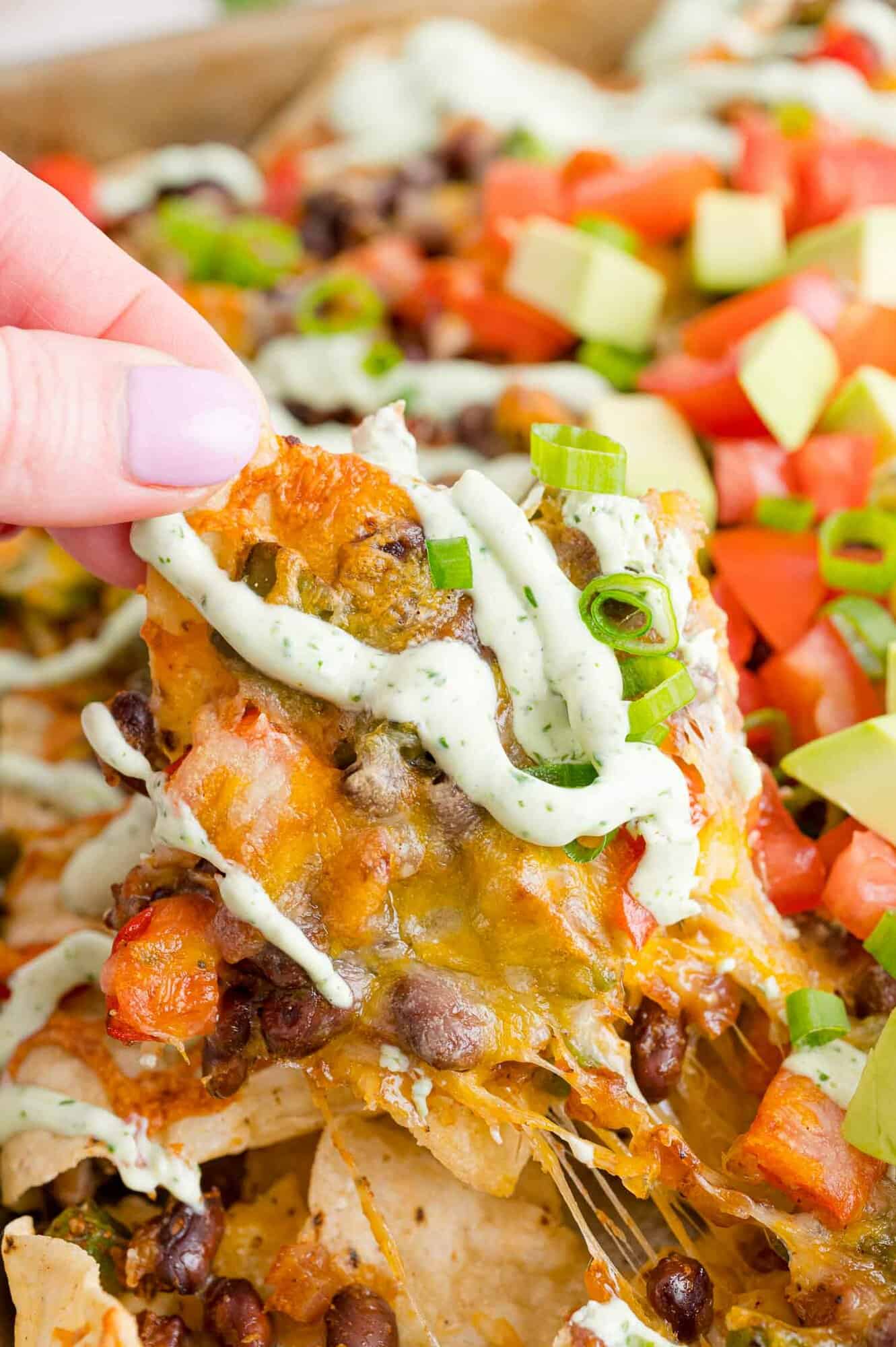 Vegetarian nachos with a drizzle, one being held in a hand.