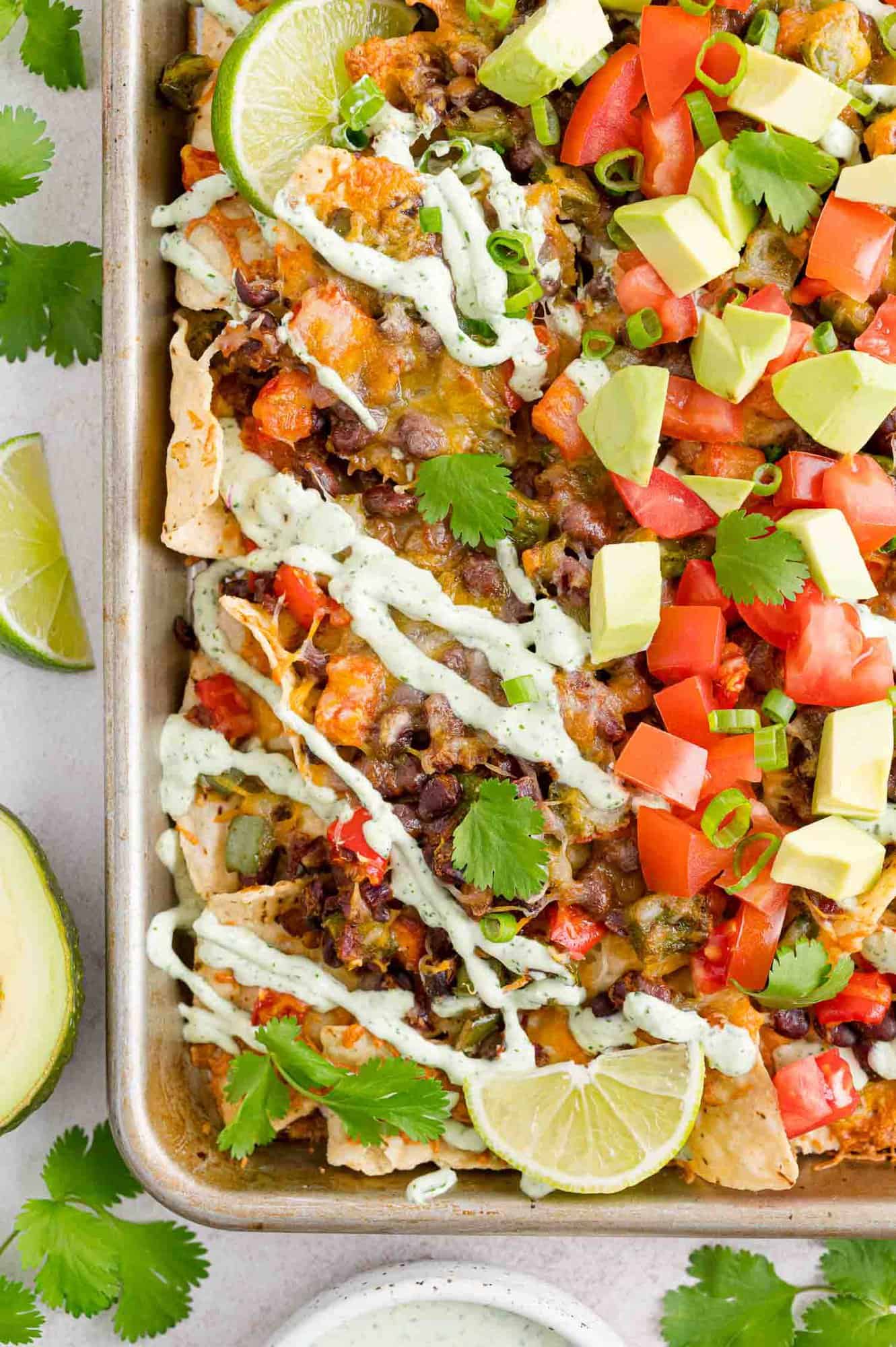 Vegetable nachos on a sheet pan with limes and sour cream drizzle.