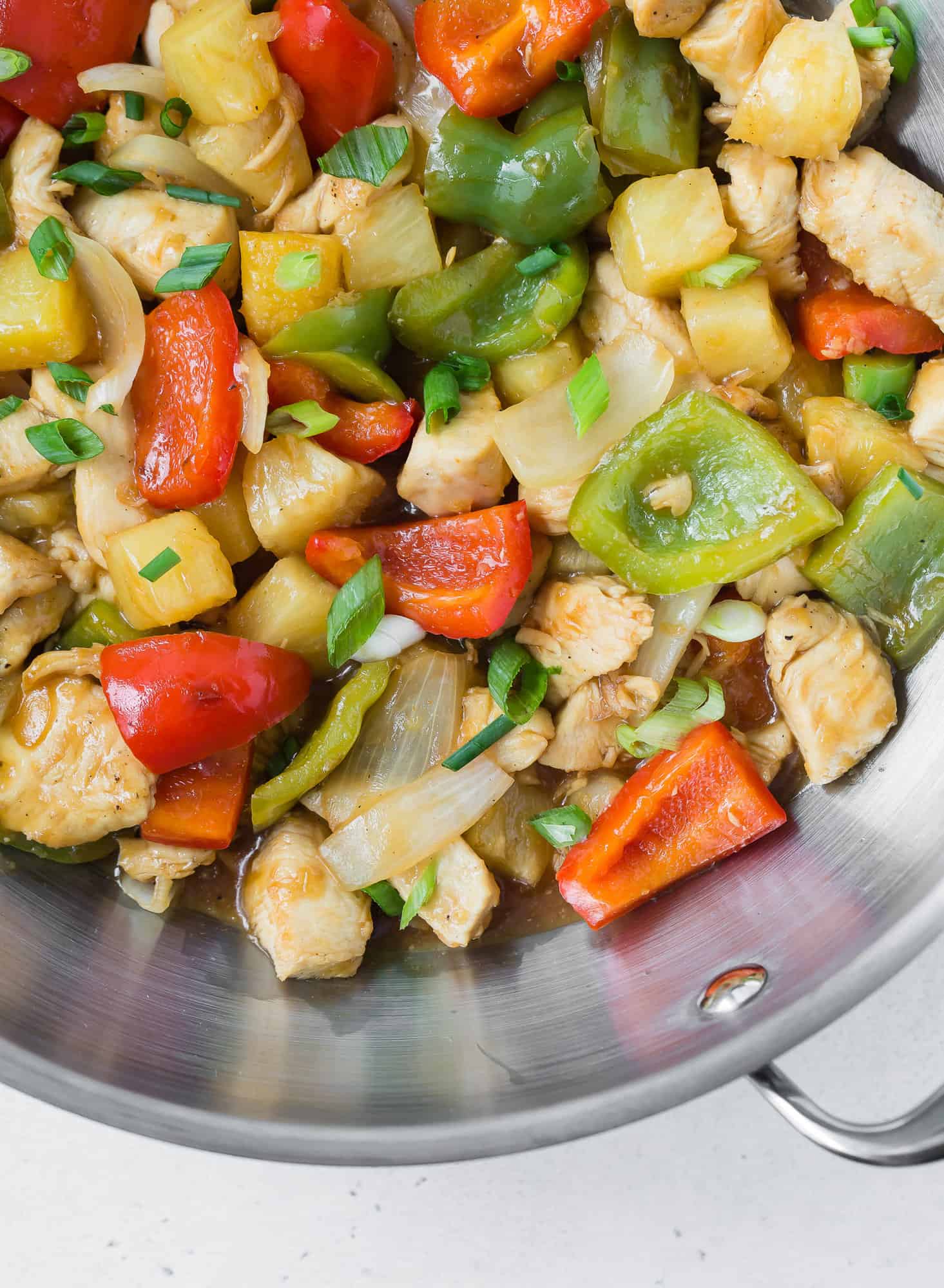 Close up of chicken stir fry with pineapple, peppers, and onions in wok.