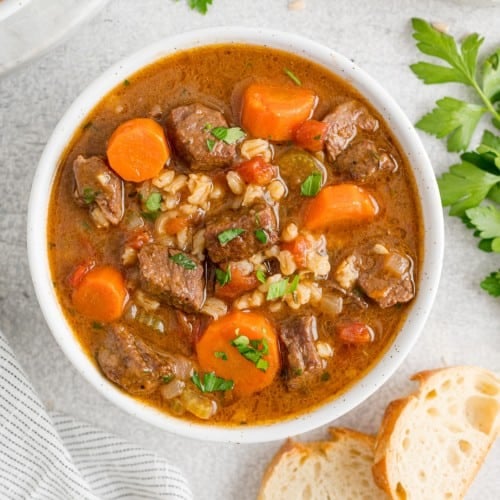 Beef barley soup in a white bowl.