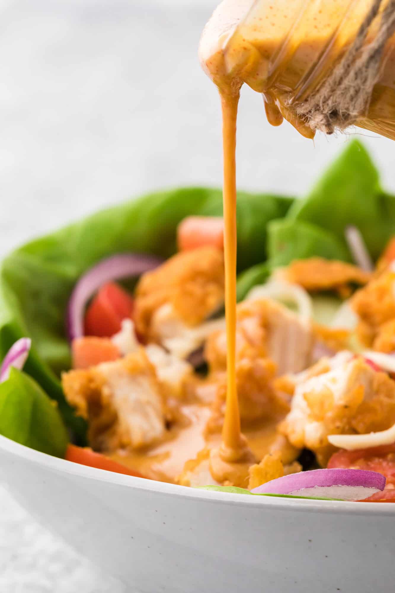 Honey mustard dressing being poured on a salad.