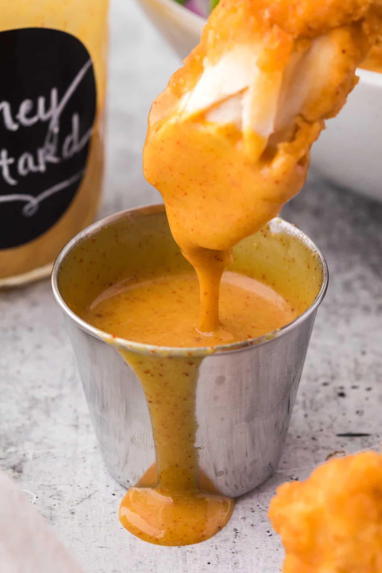 Chicken tender being dipped in honey mustard dressing.