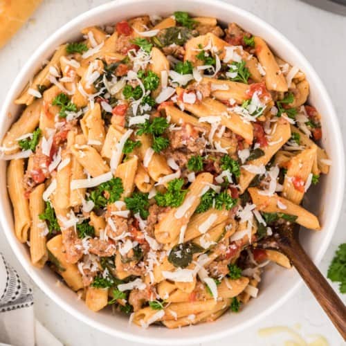 Instant Pot pasta with sausage, spinach, tomatoes, in white bowl.