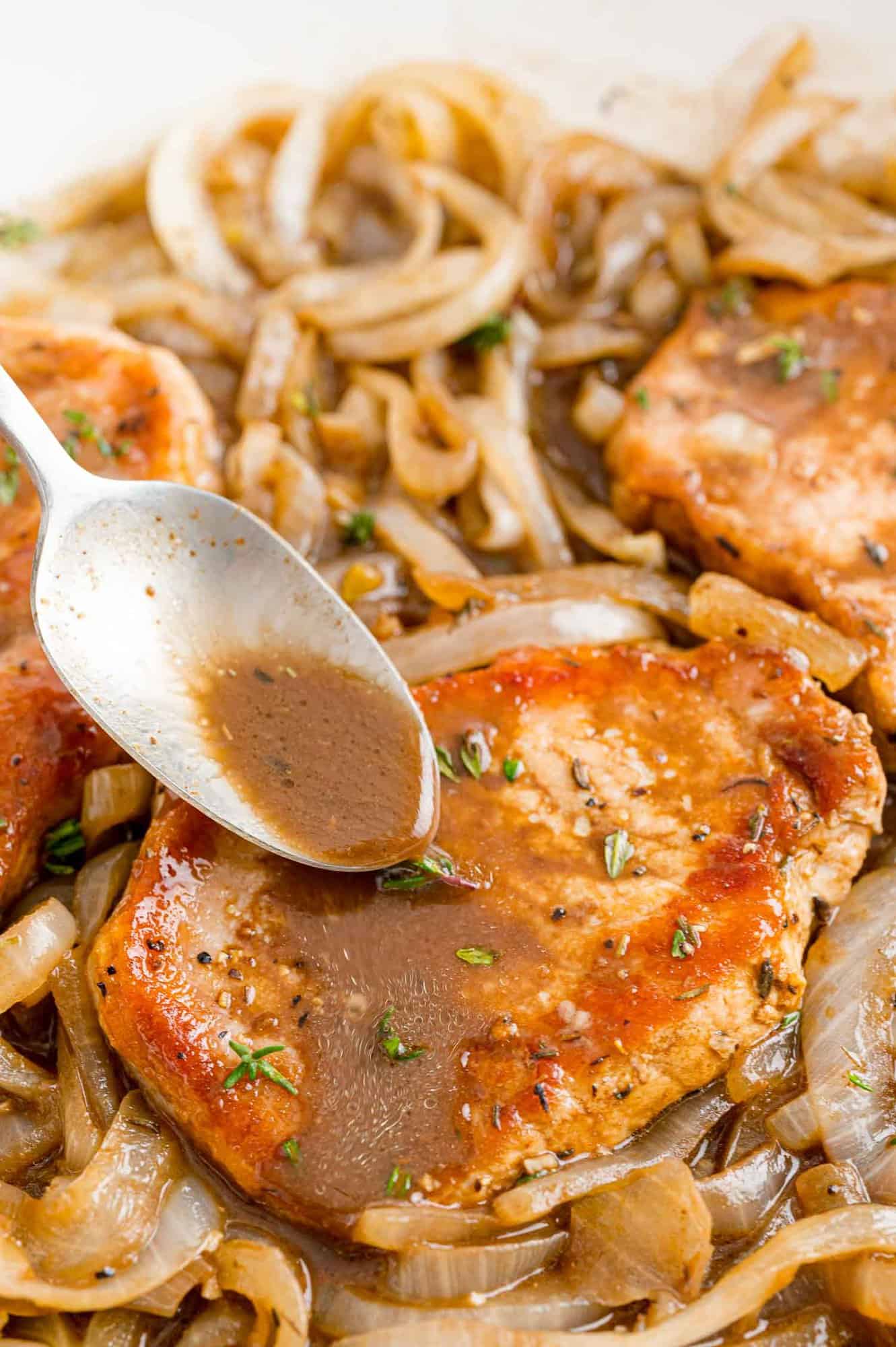 Balsamic sauce being spooned onto a pork chop and caramelized onions.