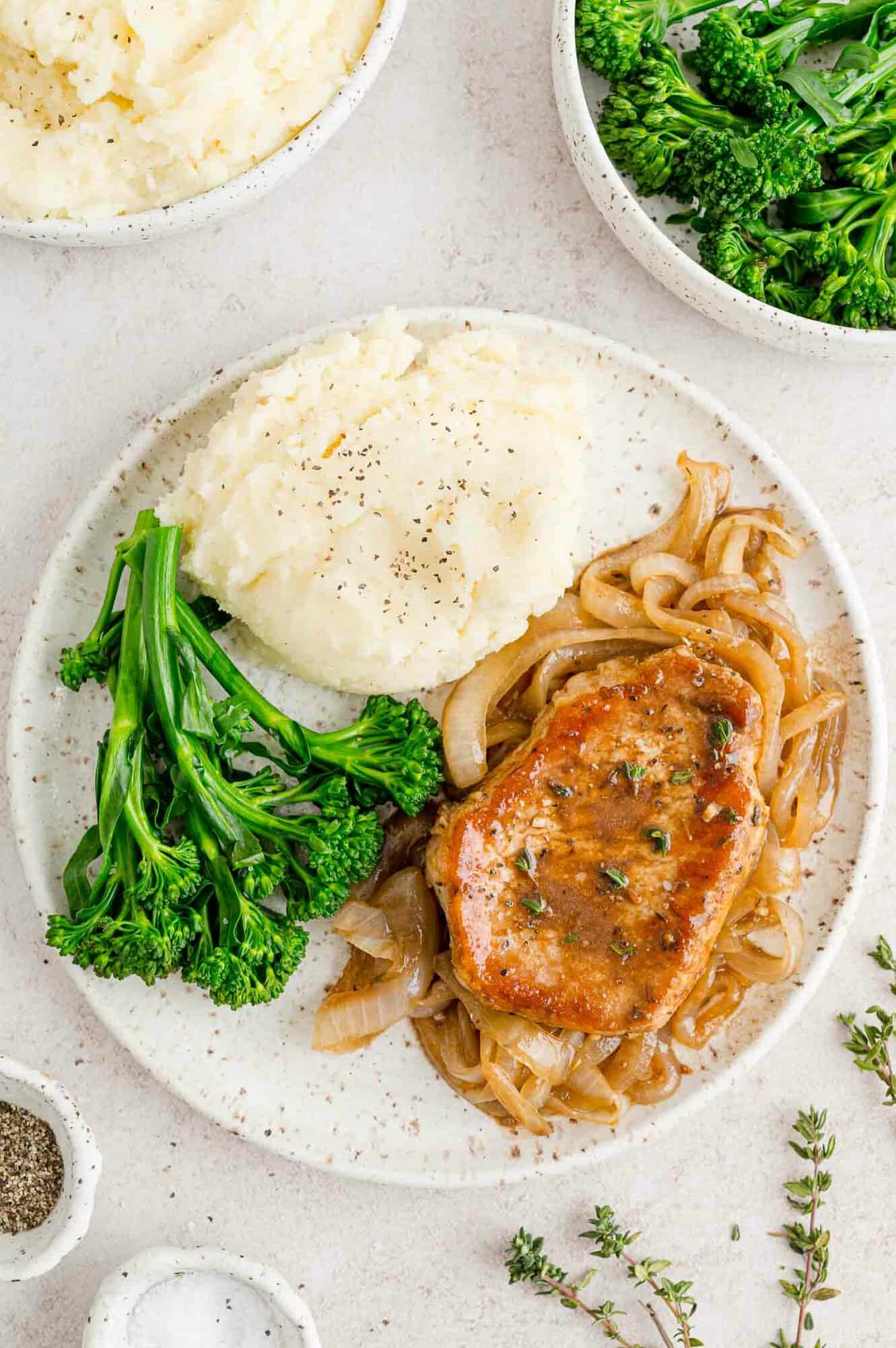 Pork chops on a plate with balsamic onions, broccolini, and mashed potatotes.