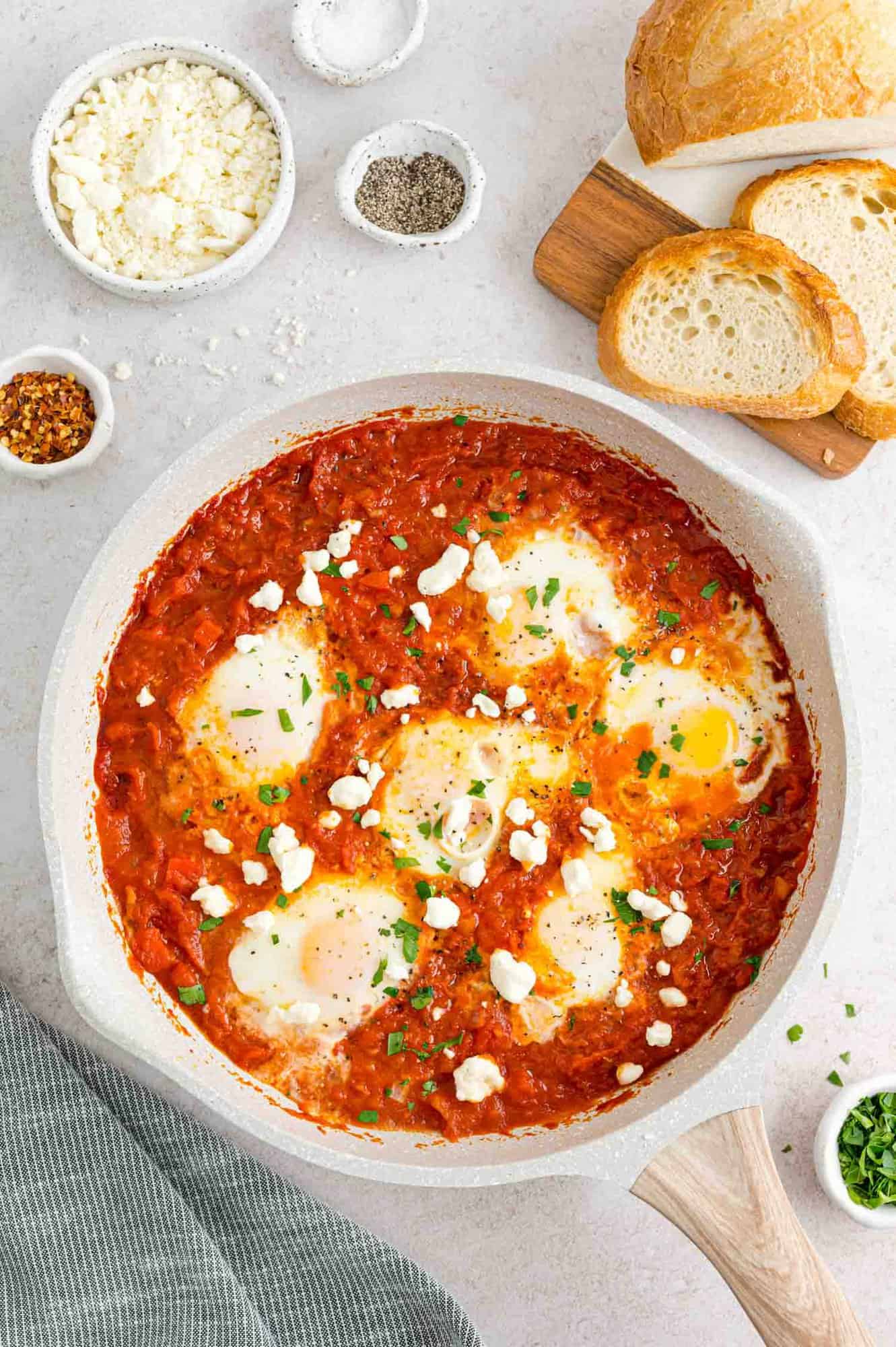 Shakshuka in a white skillet surrounded by bread slices.