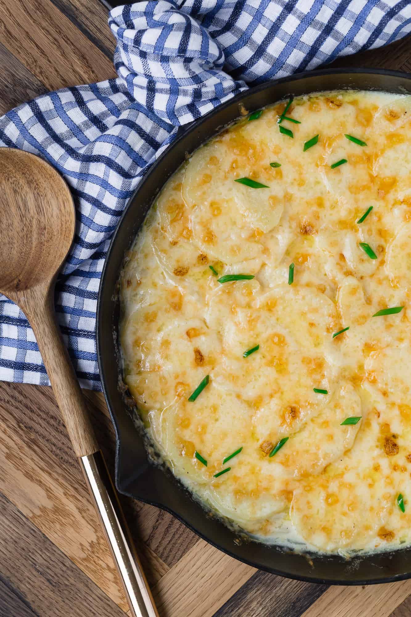 Overhead view of scalloped potatoes in a black pan.