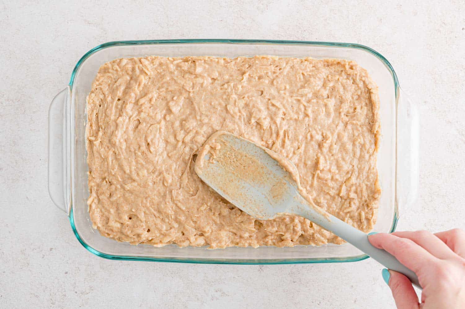 Apple spice cake batter being spread into a glass baking dish.