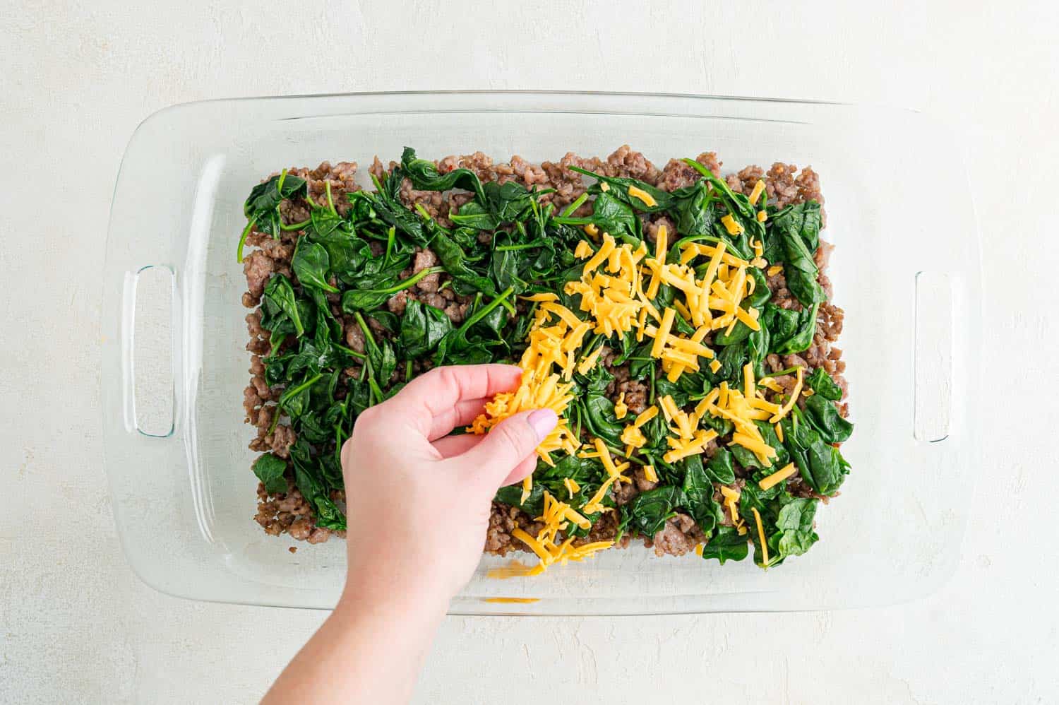 Cheese being added to casserole dish.