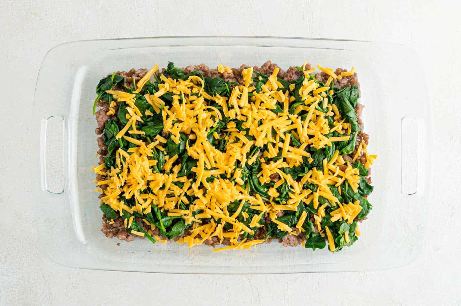 Sausage, spinach, and cheese in a casserole dish.