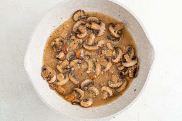 Sauteed mushrooms in a marsala wine broth in a skillet.