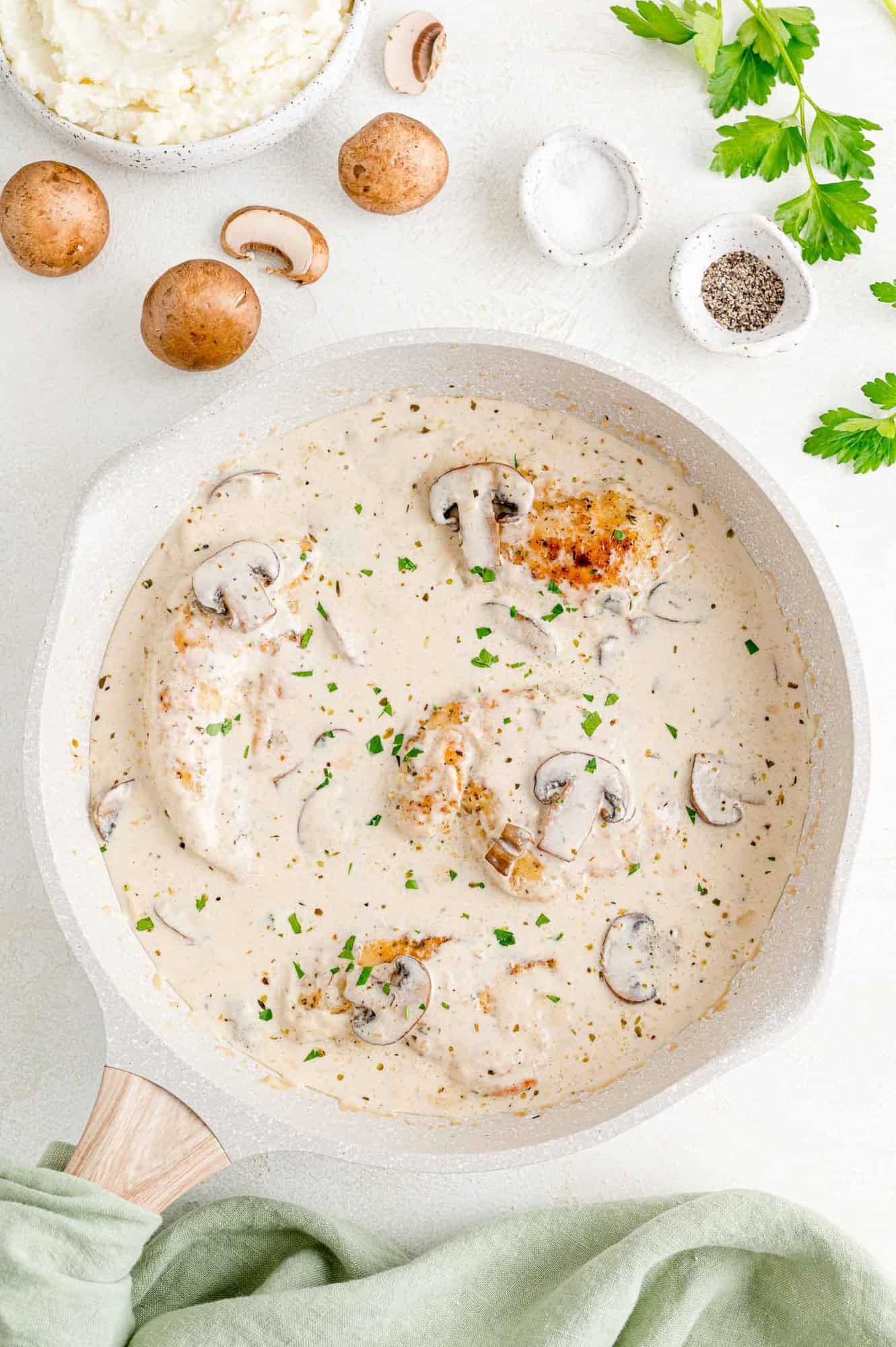 Pan-fried chicken cutlets in a skillet with mushrooms in creamy marsala sauce.