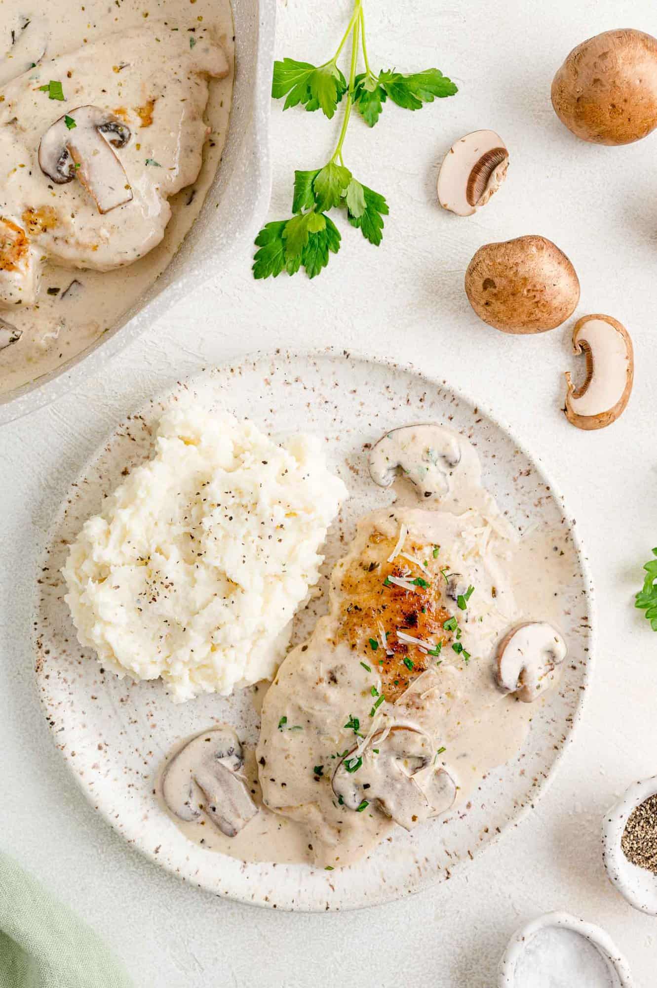 A serving of chicken marsala on a white plate next to mushrooms and mashed potatoes.