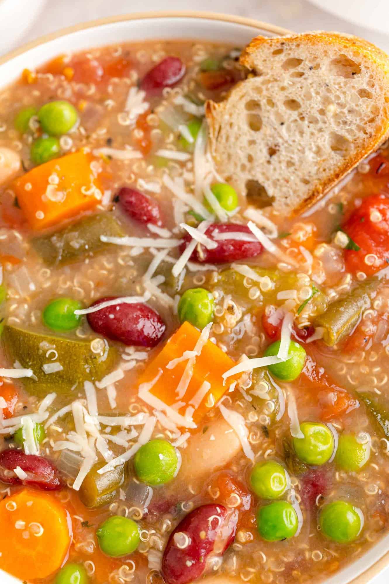 Close up of minestrone soup with a slice of bread in it.