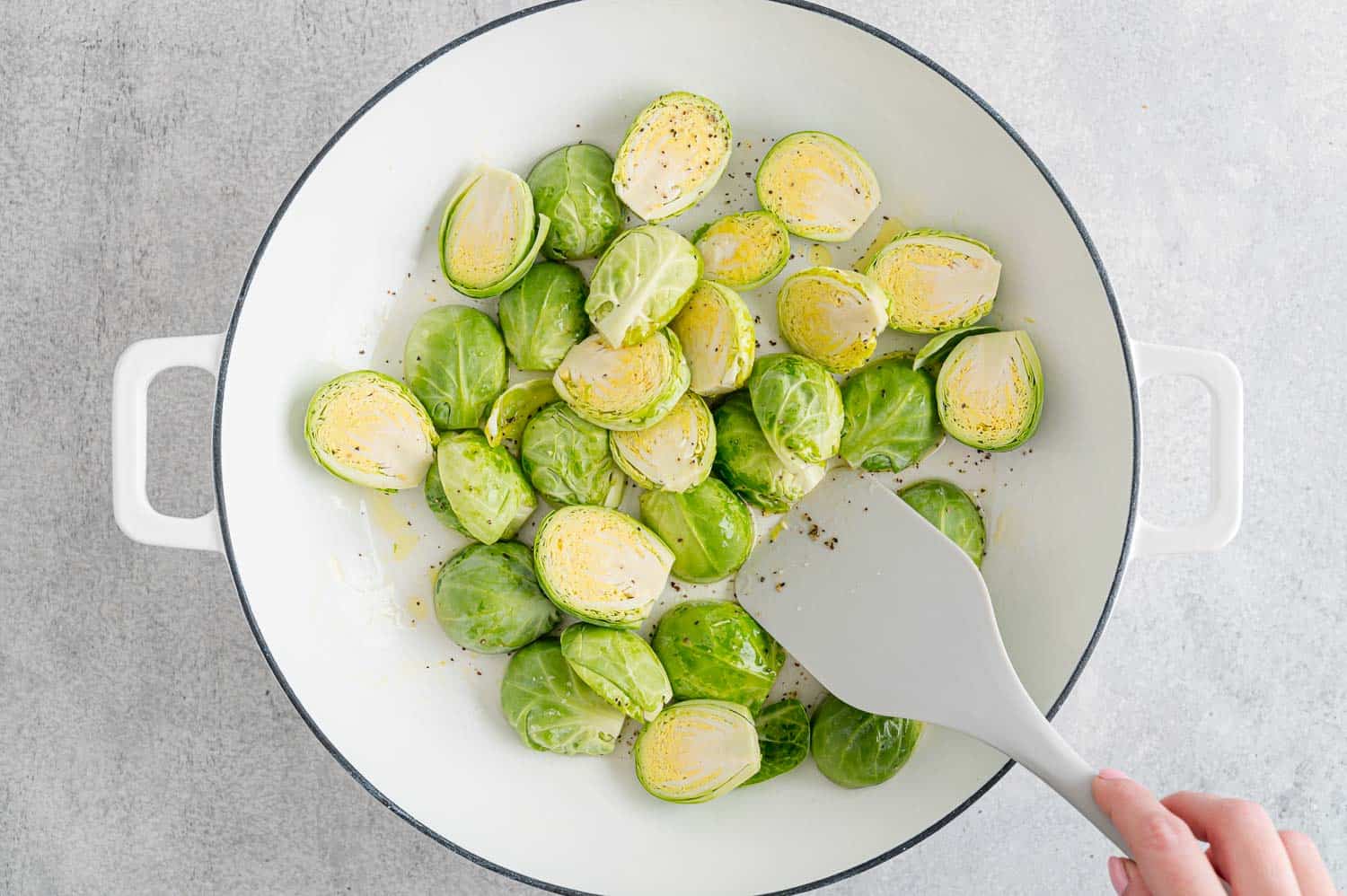 Brussels sprouts being cooked in a white frying pan.