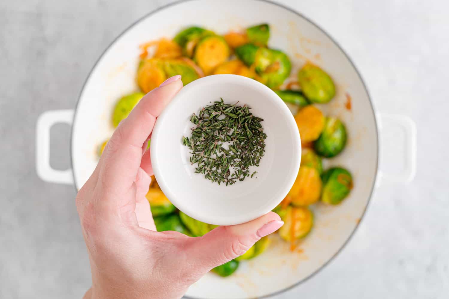 Fresh thyme being added to sautéed Brussels sprouts.