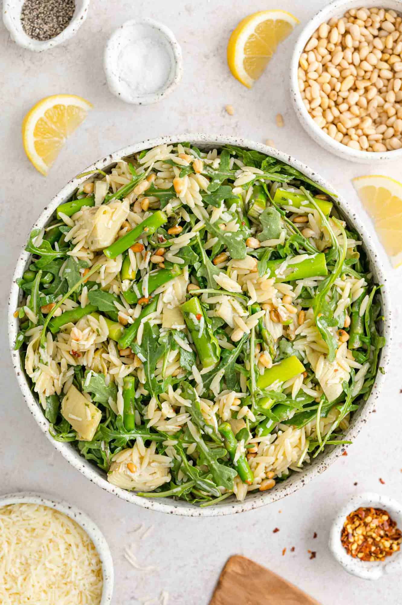 Spring orzo salad with individual ingredients surrounding bowl.