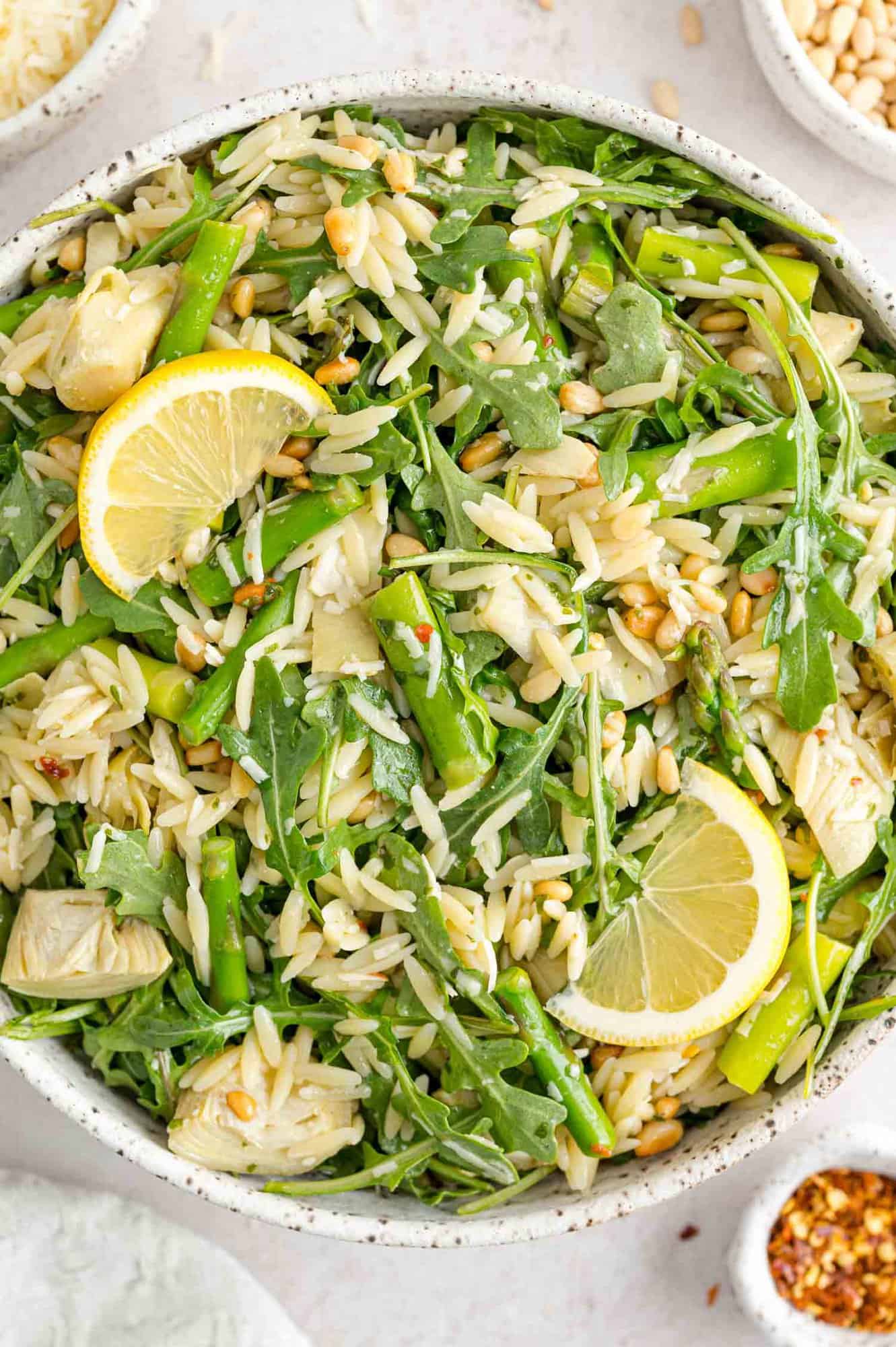 Orzo salad with asparagus, lemon, and pine nuts in large white bowl.