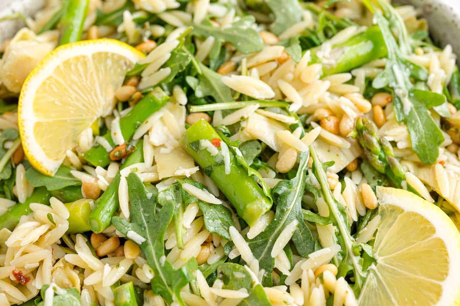 Close up view of orzo salad garnished with lemon wedges.