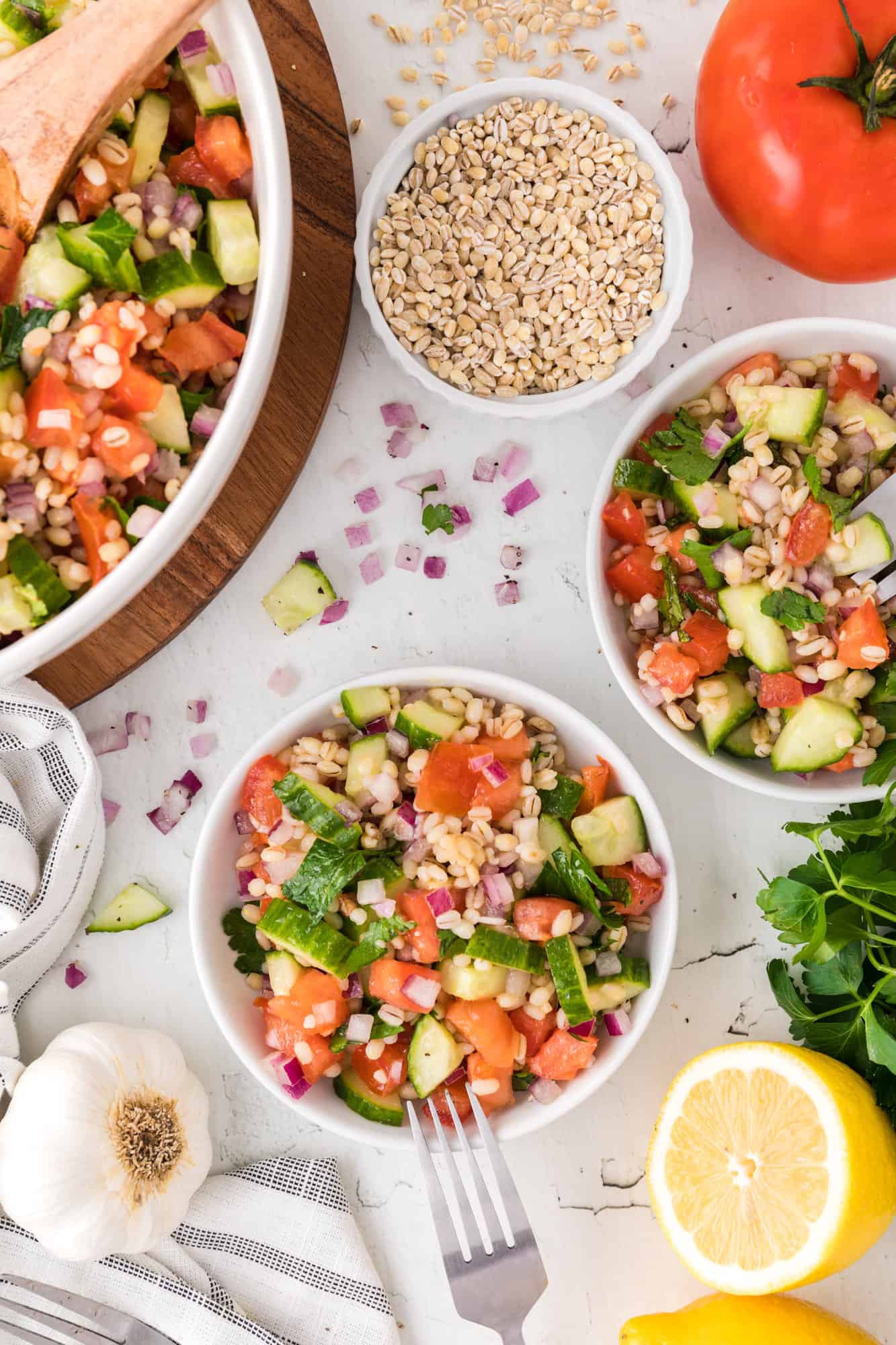 Multiple bowls of barley salad, with fresh ingredients nearby.