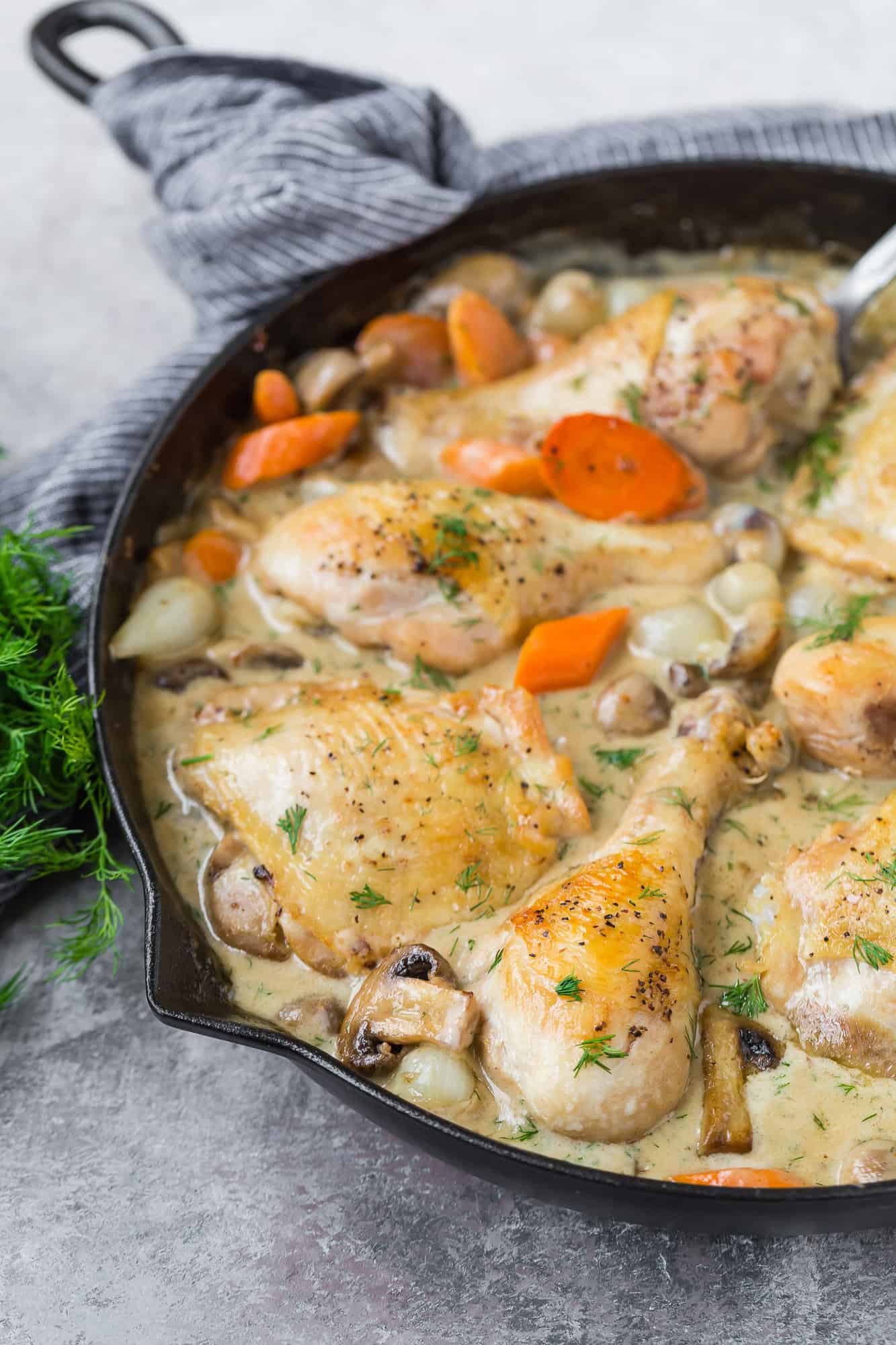 Browned chicken in a pan with gravy and vegetables.
