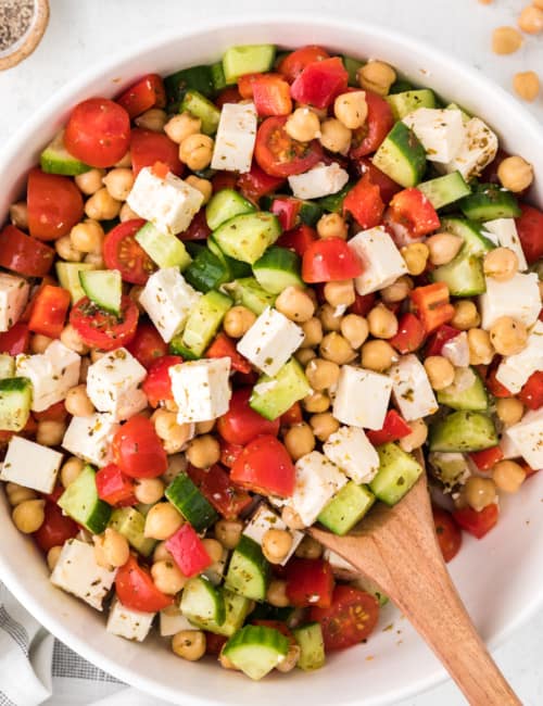 Chopped Greek salad in a white bowl with a wooden spoon.