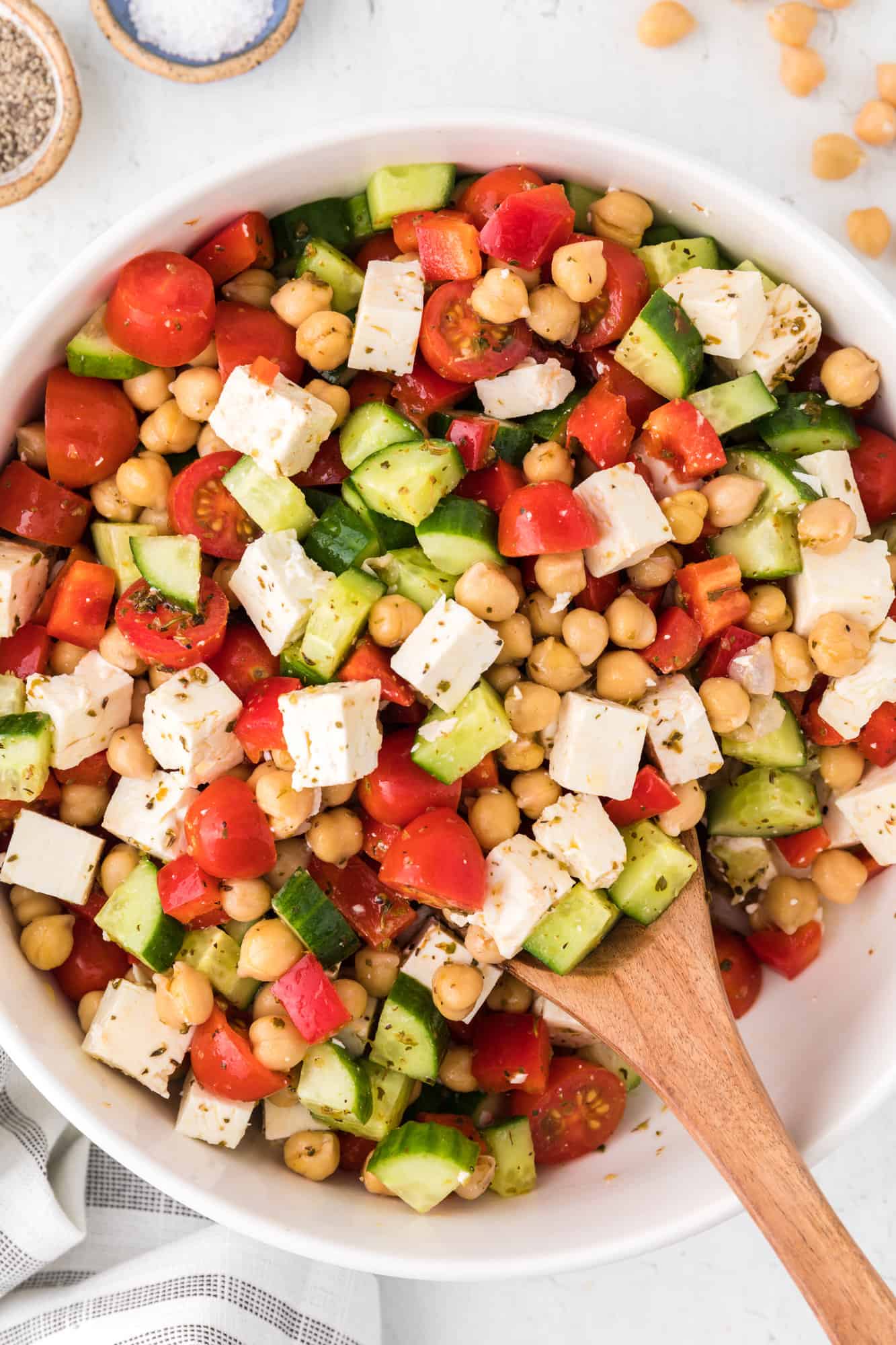 Chopped Greek salad in a white bowl with a wooden spoon.