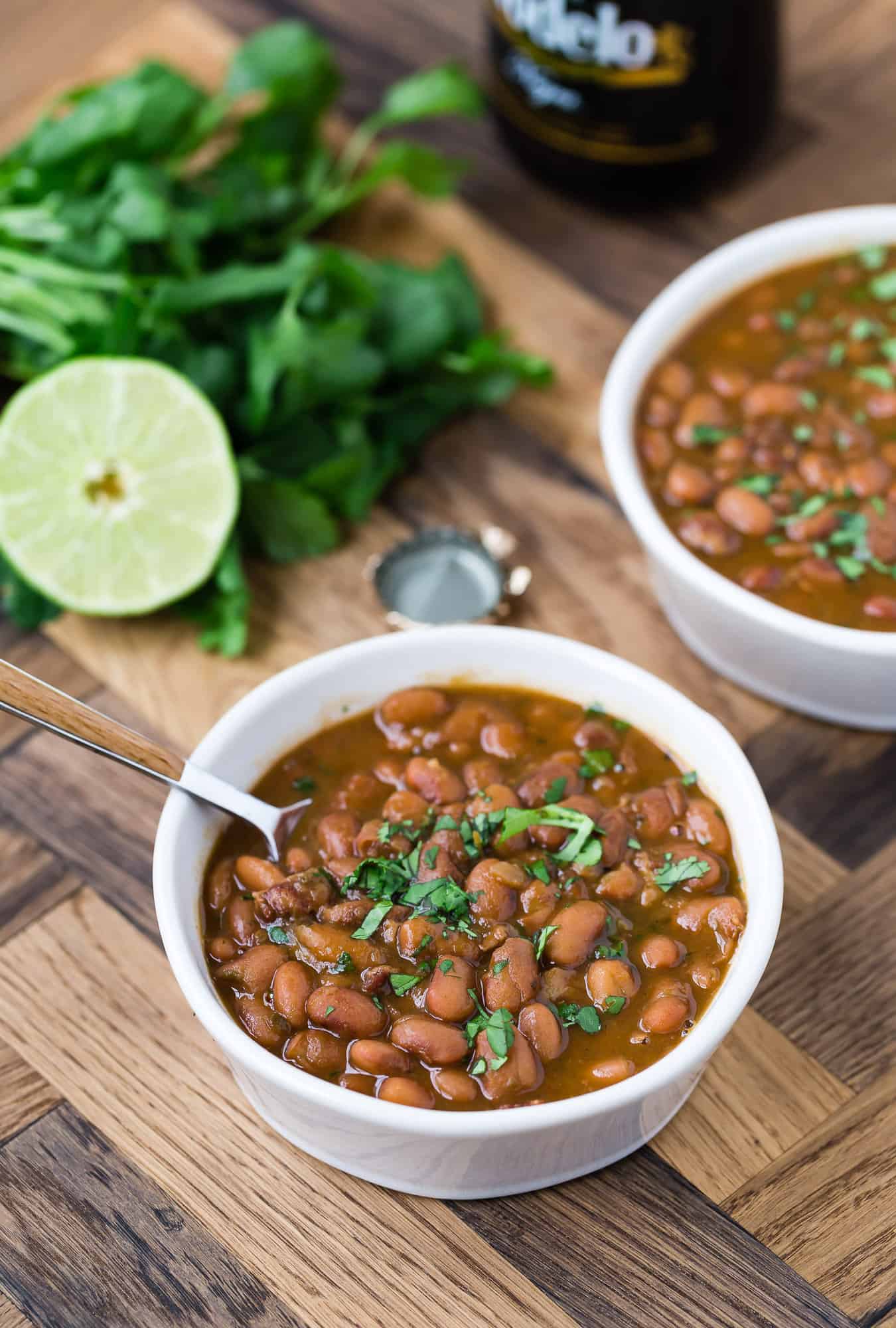 Beans, broth, and cilantro in two white bowls with spoons.