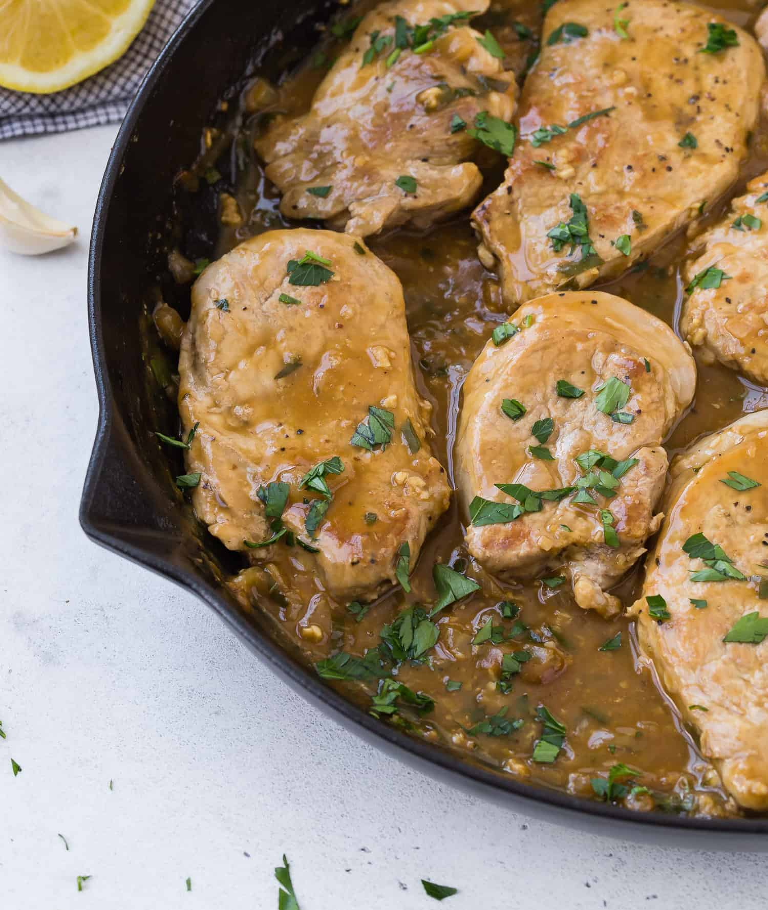 Pork in black skillet, with sauce, garnished with parsley.