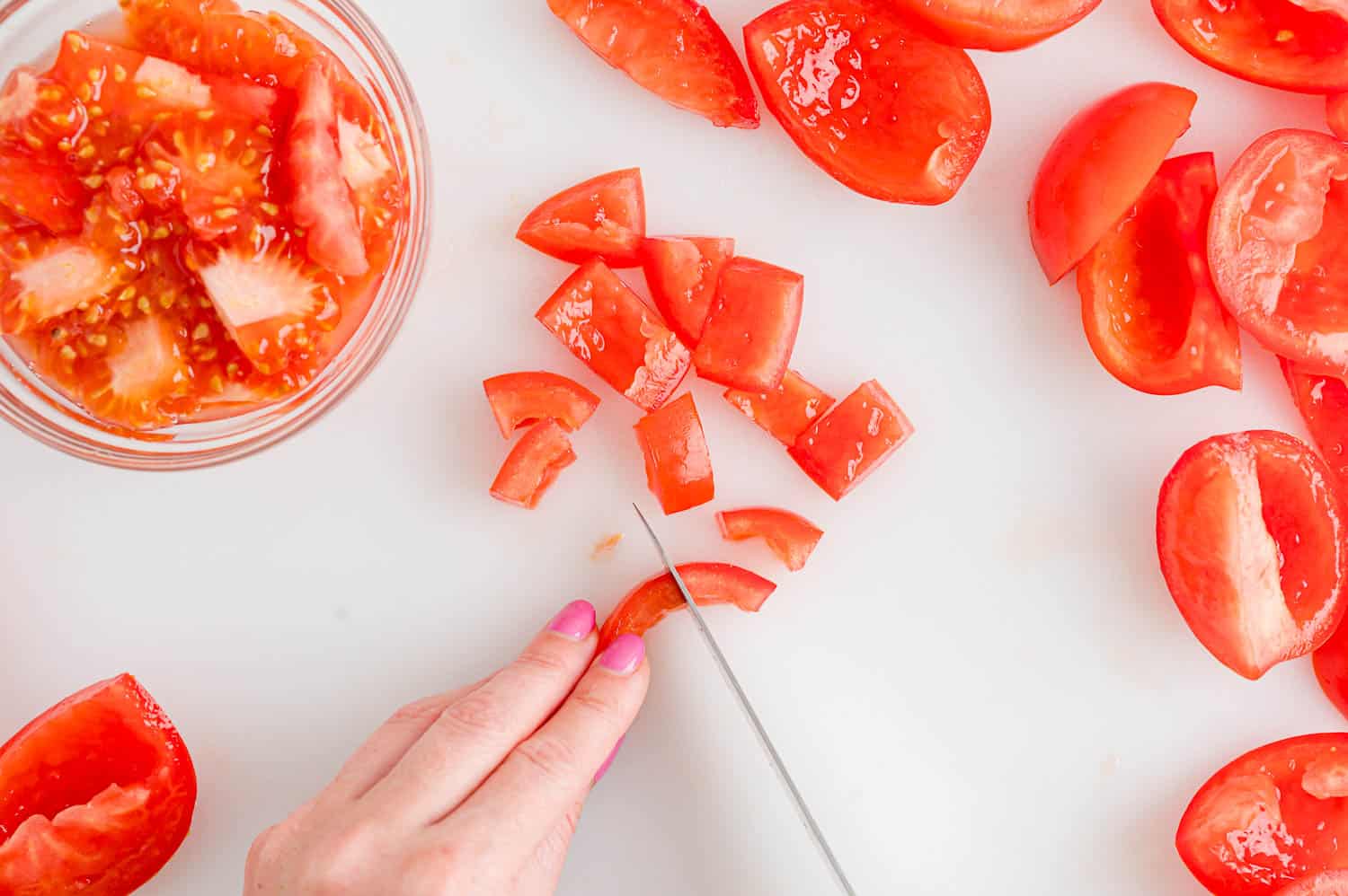 A hand using a knife to dice up deseeded and chopped fresh tomatoes.