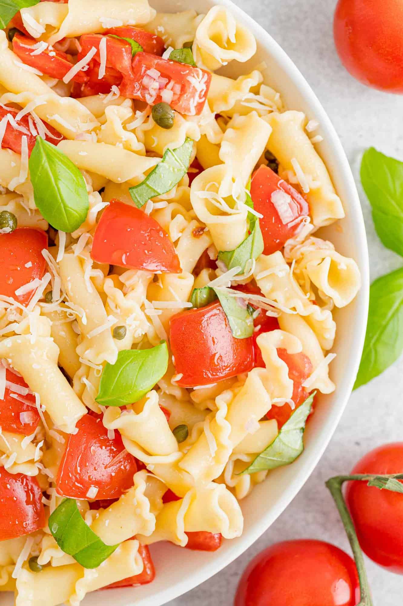 Overhead close up view of a bowl of fresh tomato pasta surrounded by scattered tomatoes.