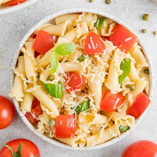 Overhead view of a bowl of fresh tomato pasta surrounded by scattered tomatoes.