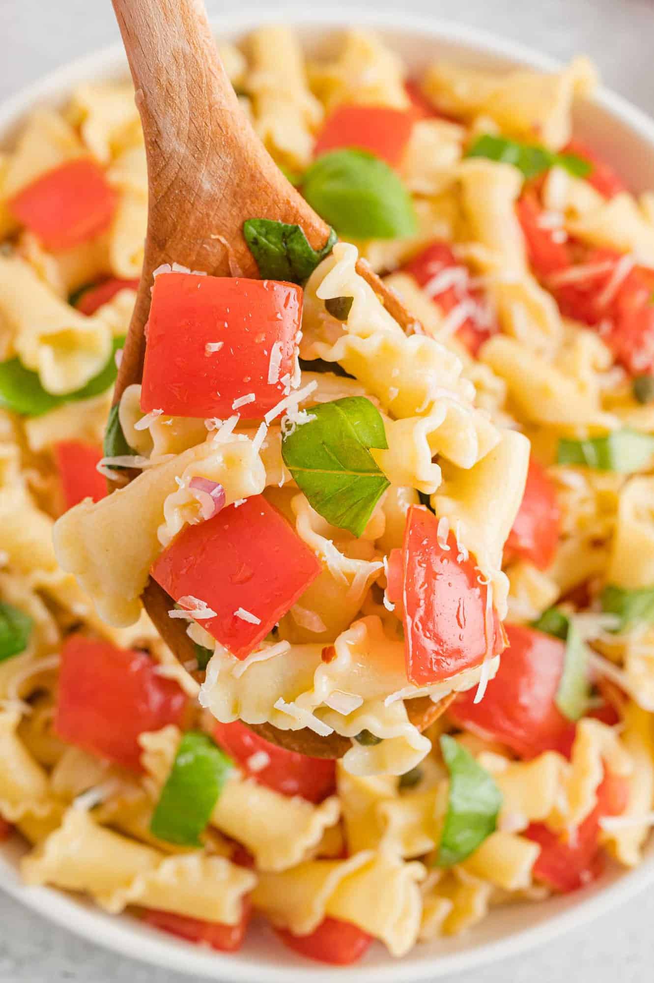 Close up of a wooden spoon scooping fresh tomato pasta from a large bowl.