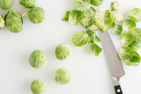 Trimmed and peeled Brussels sprouts on a countertop next to discarded leaves and a sharp knife.