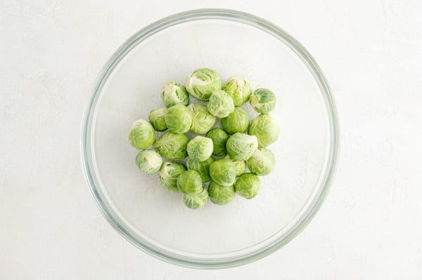 Uncooked Brussels sprouts in a glass bowl.