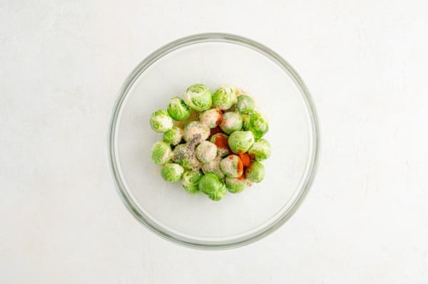 Seasonings added to microwaved Brussels sprouts in a glass bowl.